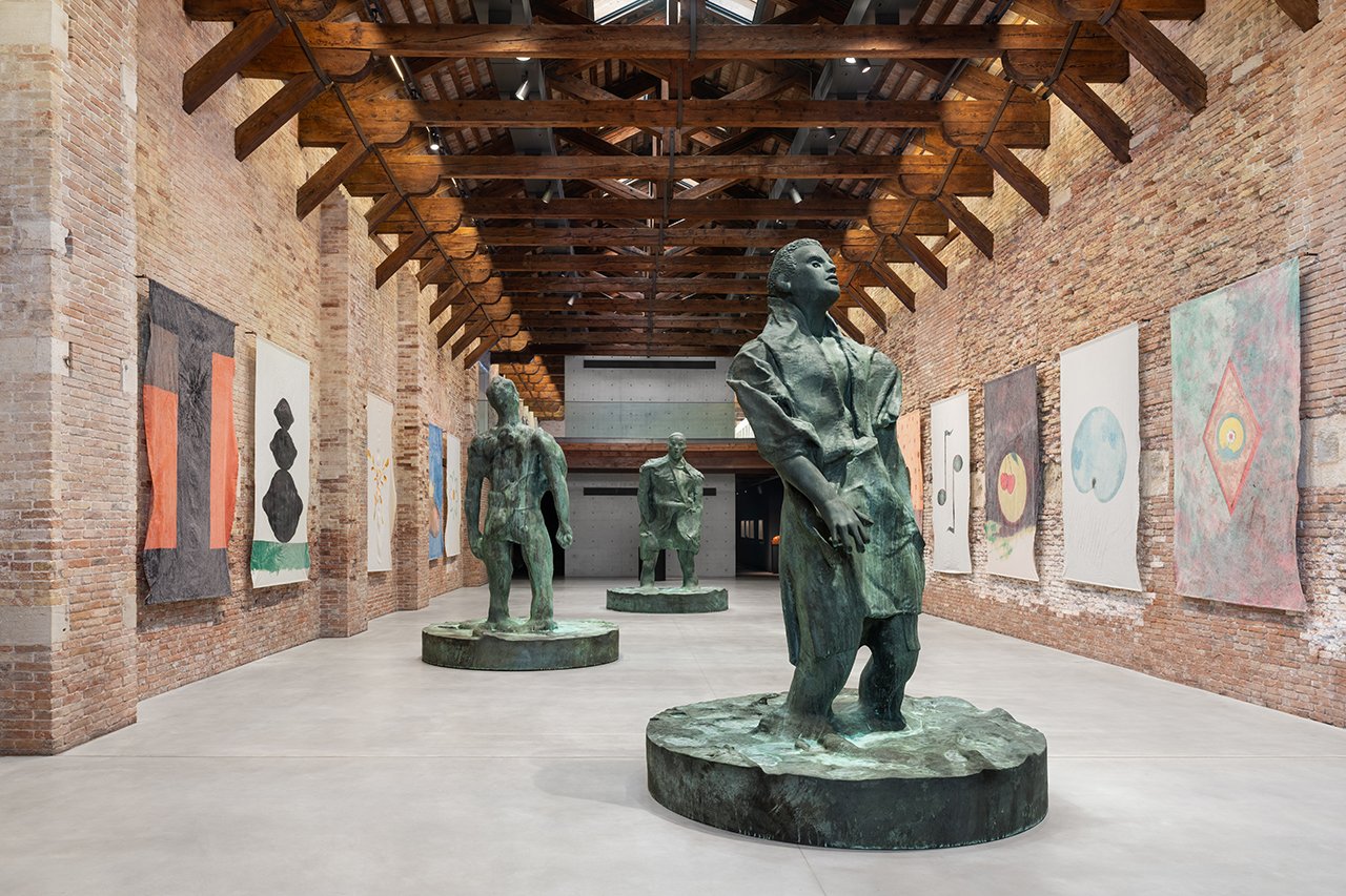 Thomas Schütte, "Mann im Wind II", 2018, Pinault Collection; "Mann im Wind I", 2018, Pinault Collection; "Mann im Wind III", 2018, Pinault Collection; "DEKA Fahnen", 1989, Courtesy the artist and Peter Freeman, Inc., New York/Paris © Thomas Schütte, by SIAE 2025. Installation view, “Thomas Schütte. Genealogies”, 2025, Punta della Dogana, Venezia. Ph. Marco Cappelletti © Palazzo Grassi - Pinault Collection